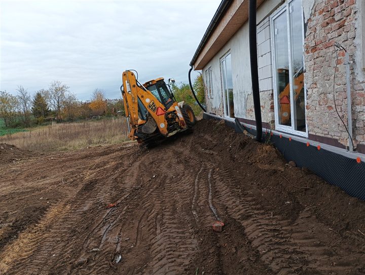 Traktorbager upravujúci terén vedľa domu